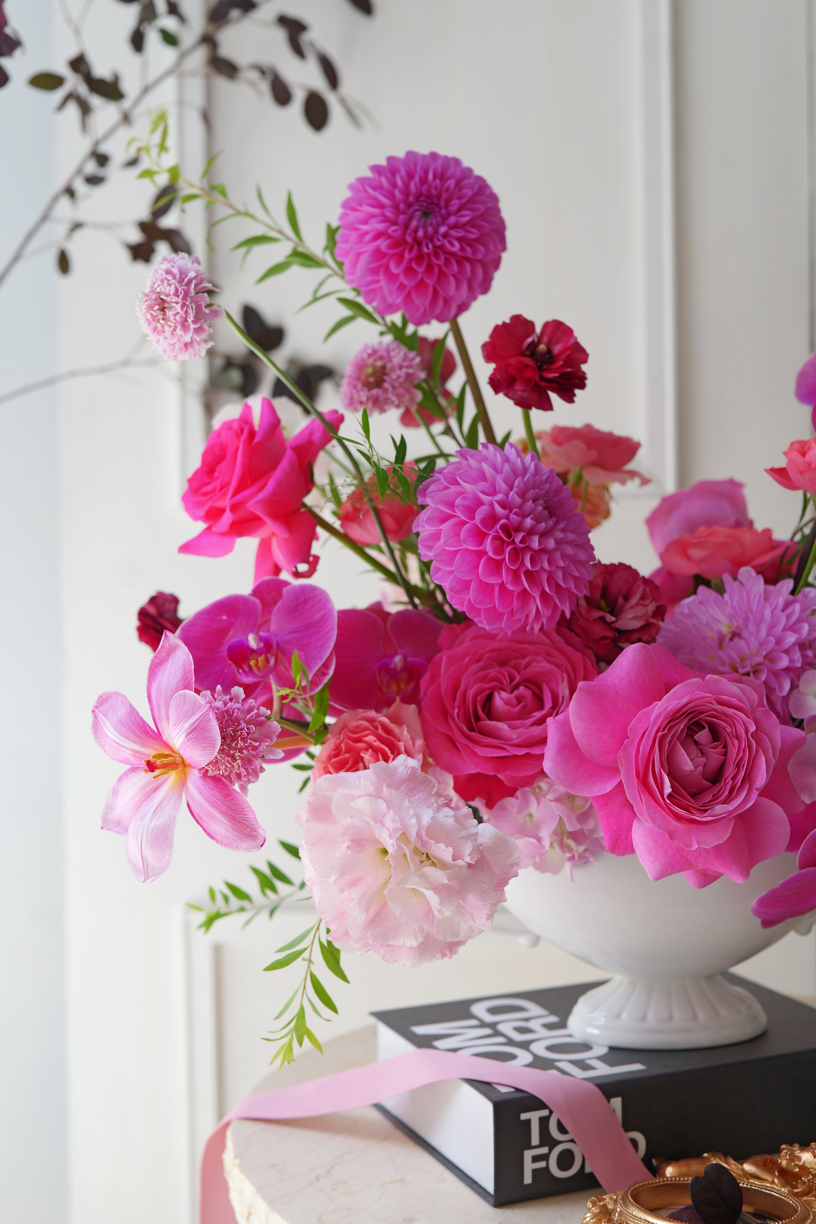 Luxury pink garden-style centerpiece with roses, orchids, dahlias, and seasonal flowers arranged in an elegant white compote vase.