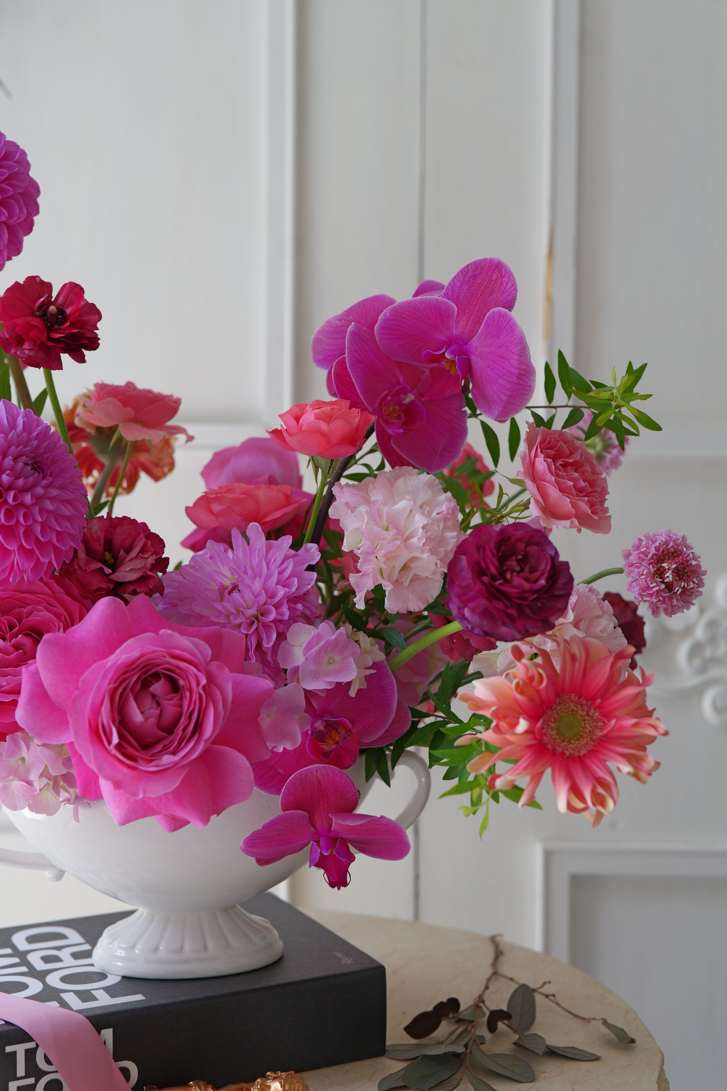 Luxury pink garden-style centerpiece with roses, orchids, dahlias, and seasonal flowers arranged in an elegant white compote vase.