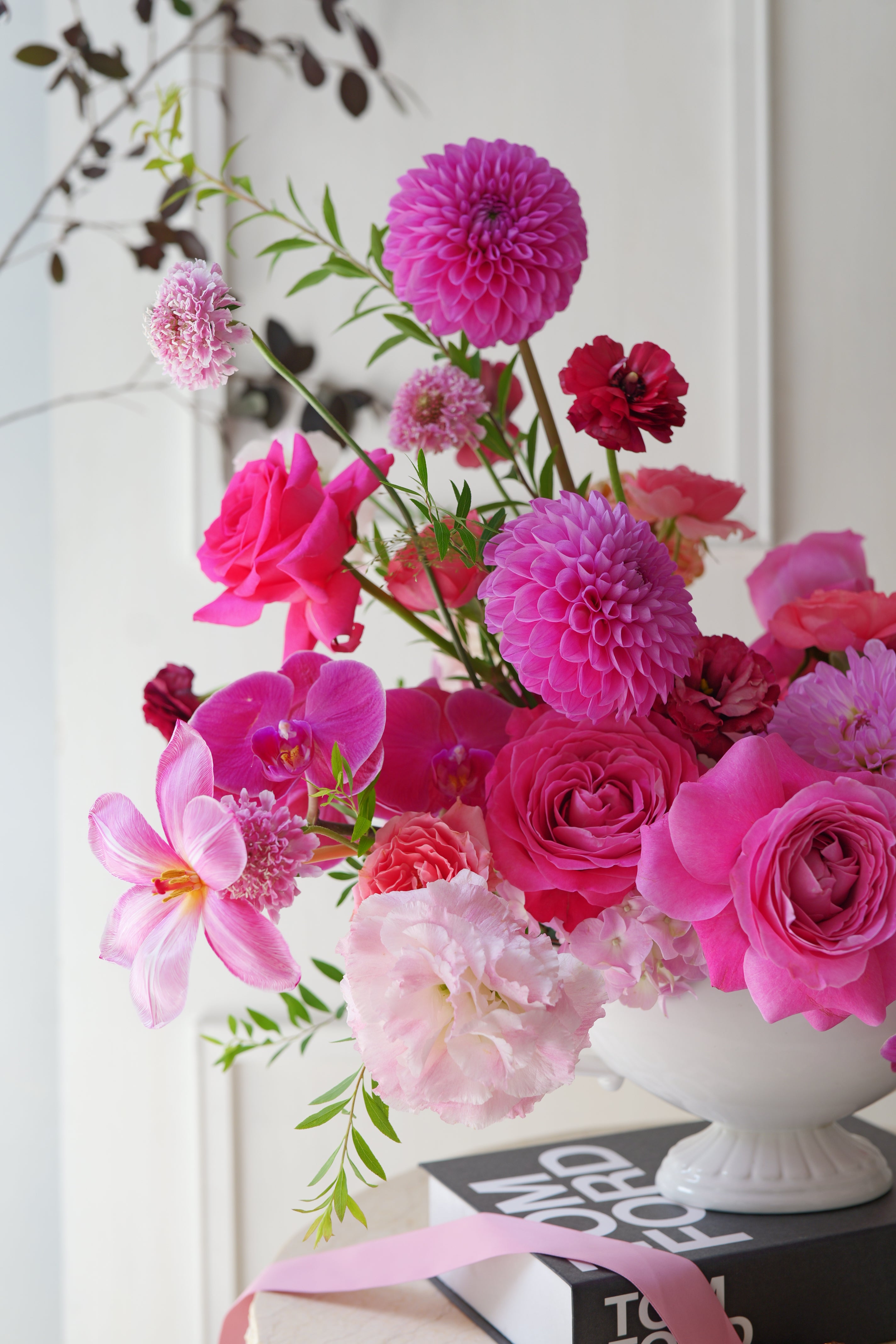 Luxury pink garden-style centerpiece with roses, orchids, dahlias, and seasonal flowers arranged in an elegant white compote vase.