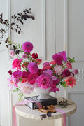Luxury pink garden-style centerpiece with roses, orchids, dahlias, and seasonal flowers arranged in an elegant white compote vase.