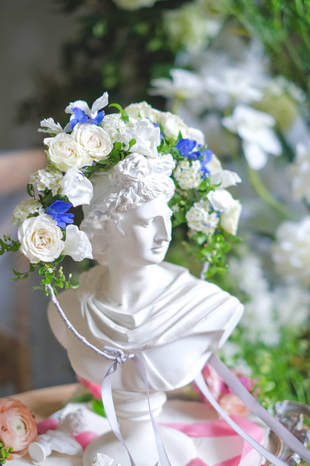 Elegant white and blue floral crown with garden roses and delphinium displayed on a classical bust