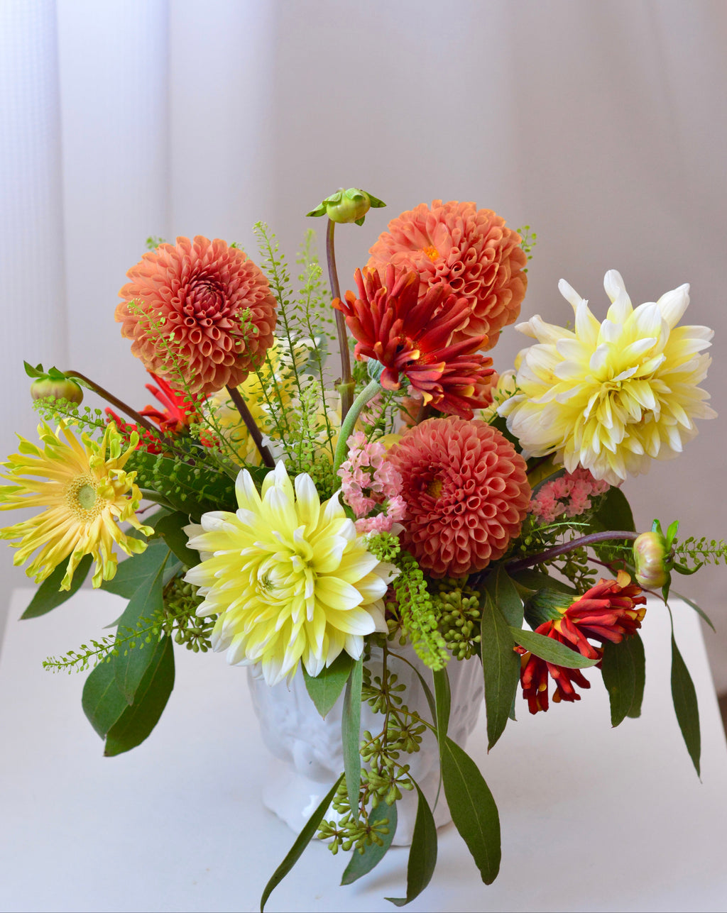 Classic garden centerpiece featuring dahlias, gerbera daisies, chrysanthemums, astilbe, seasonal blooms, and greenery arranged in a white vase.