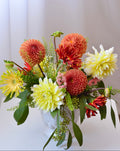 Classic garden centerpiece featuring dahlias, gerbera daisies, chrysanthemums, astilbe, seasonal blooms, and greenery arranged in a white vase.