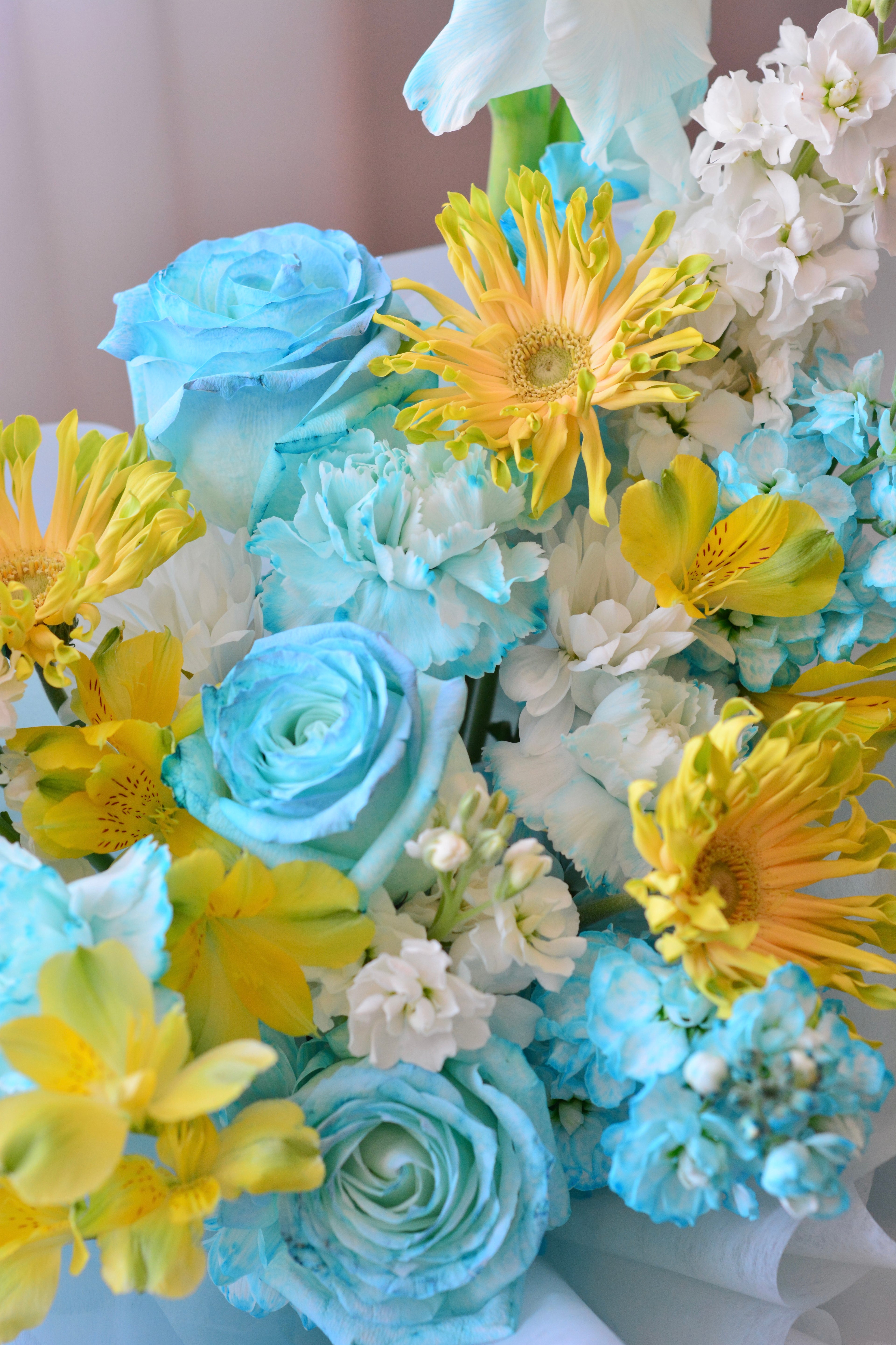 Blue Lemonade bouquet featuring tinted blue roses, yellow gerbera daisies, gladiolus, stock flowers, chrysanthemums, and seasonal blooms wrapped in soft blue paper.
