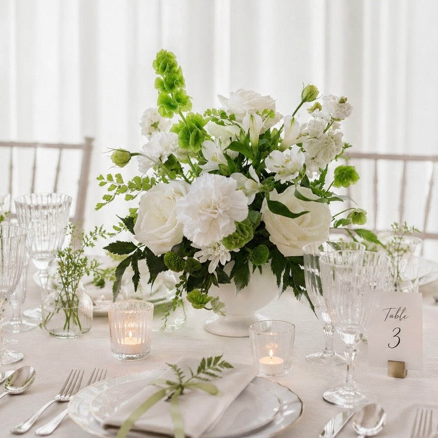 Elegant white wedding centerpiece with roses and seasonal flowers for wedding reception tables.