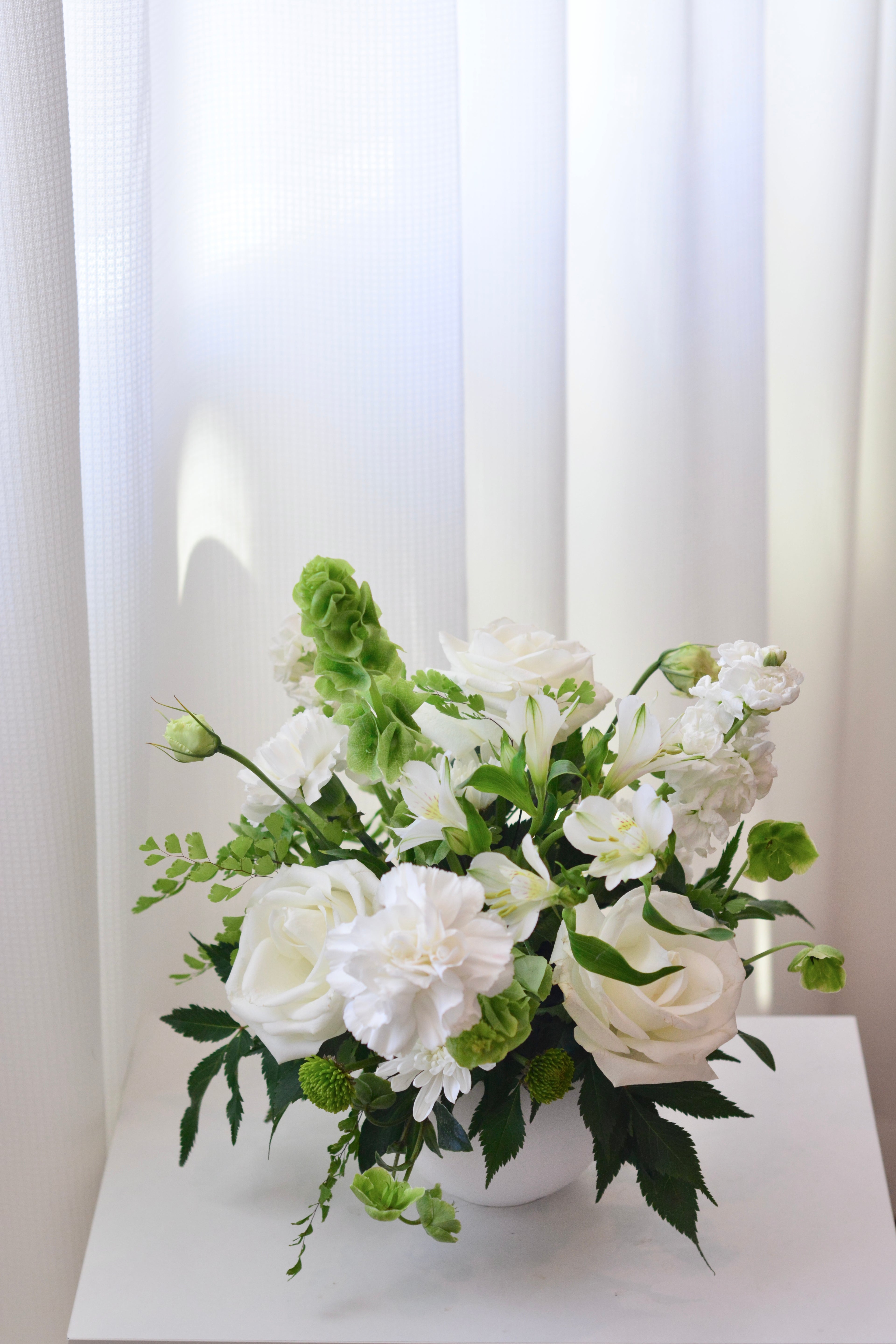 Elegant white wedding centerpiece with roses and seasonal flowers for wedding reception tables.