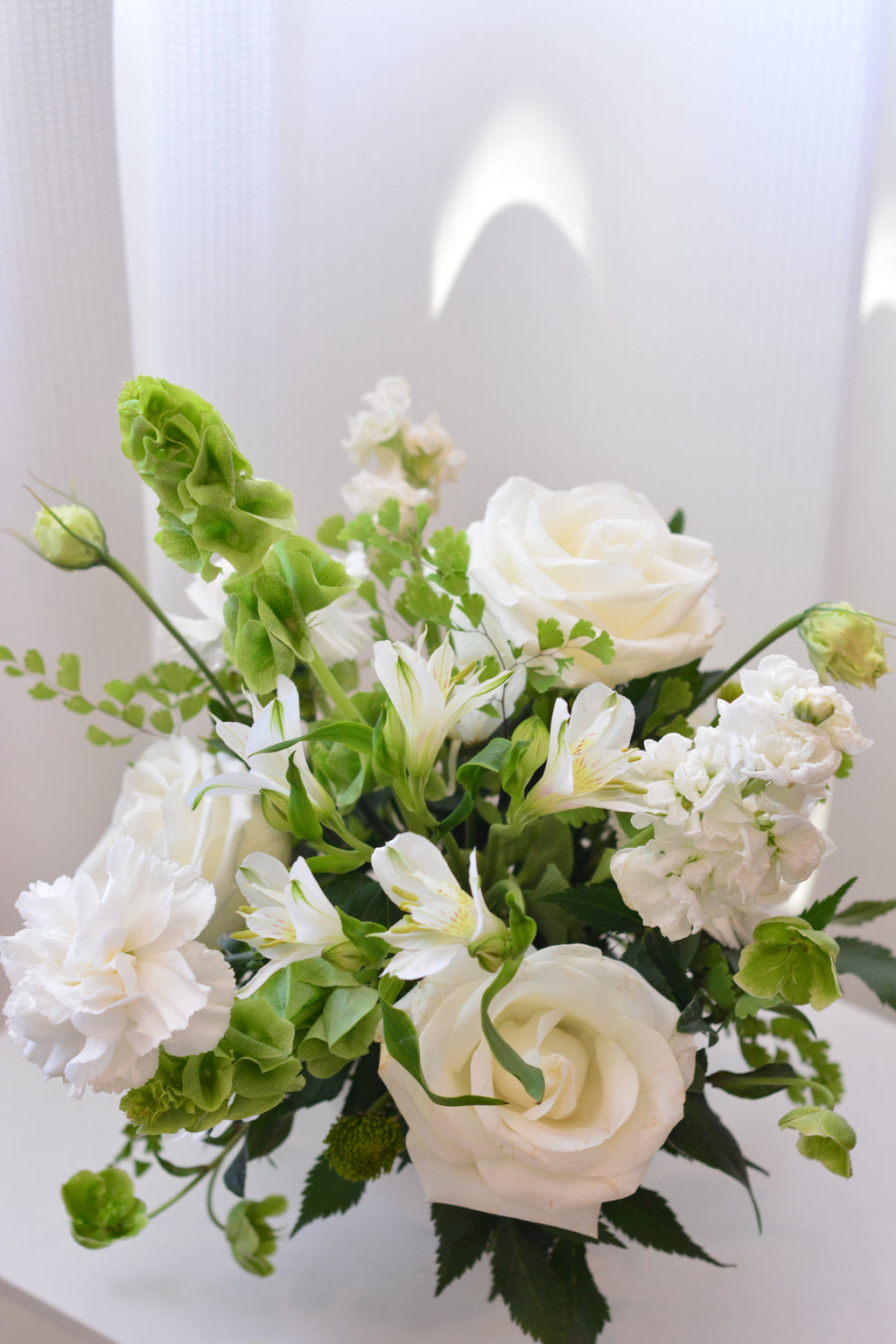 Elegant white wedding centerpiece with roses and seasonal flowers for wedding reception tables.