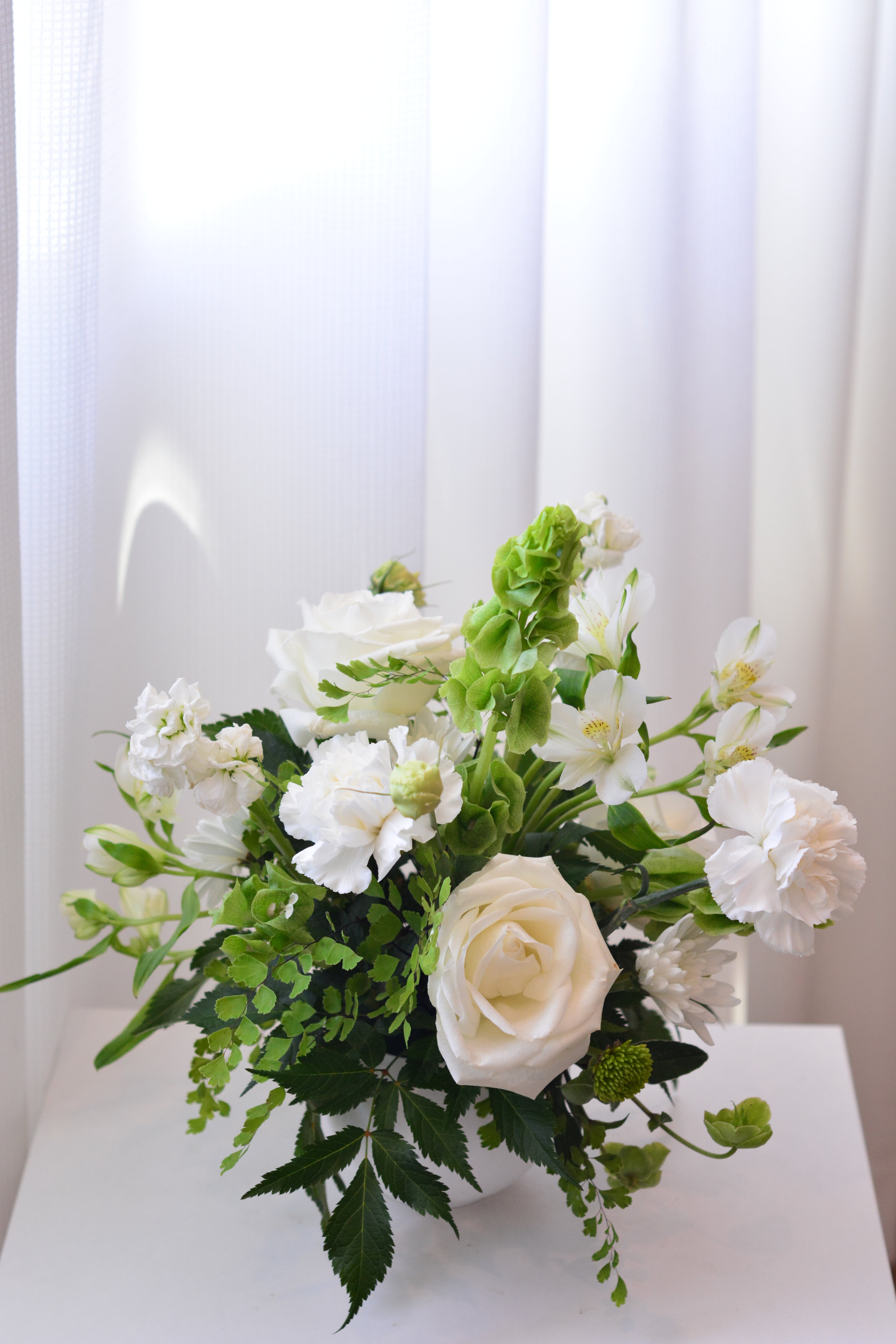 Elegant white wedding centerpiece with roses and seasonal flowers for wedding reception tables.